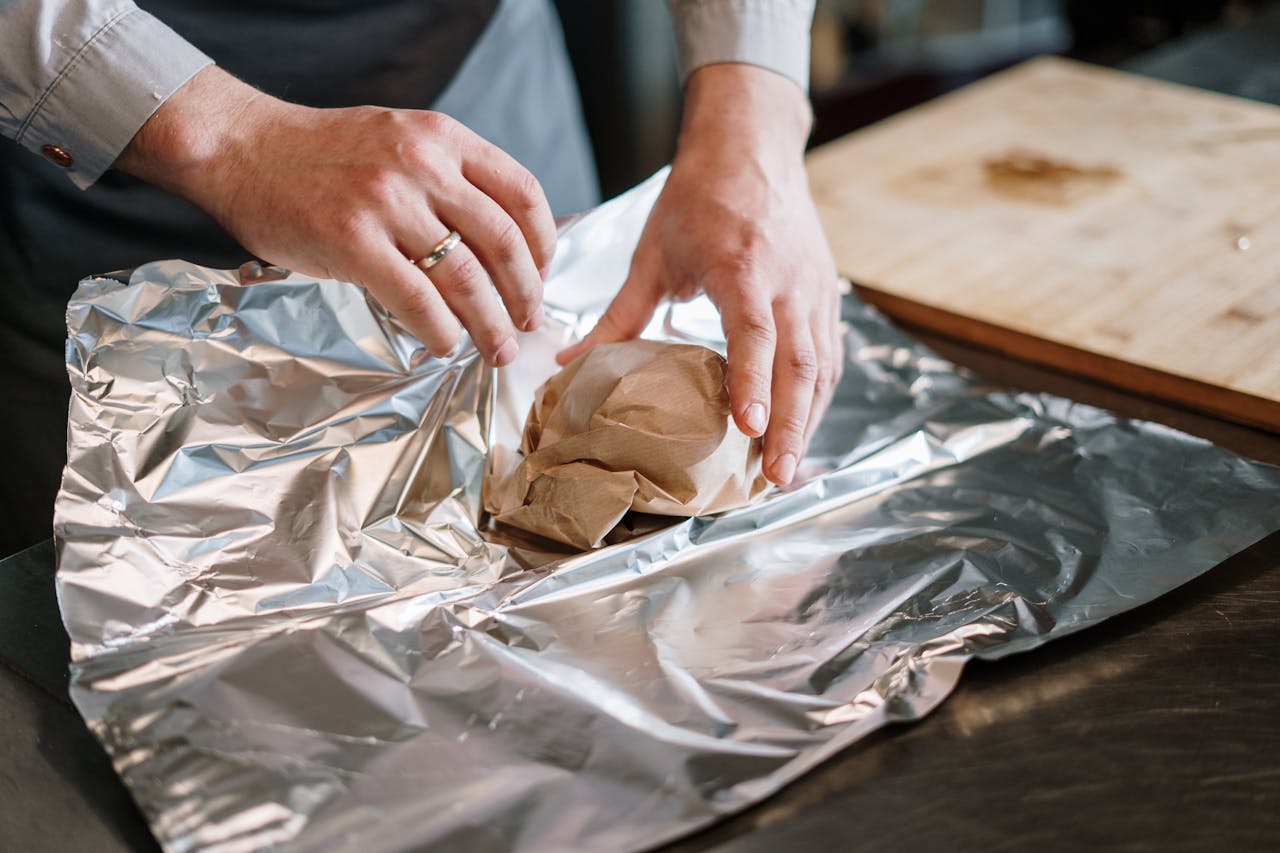 Close-up of a chef's hands wrapping food ingredients in foil for cooking.